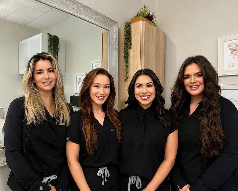 Four women in black scrubs smiling together.