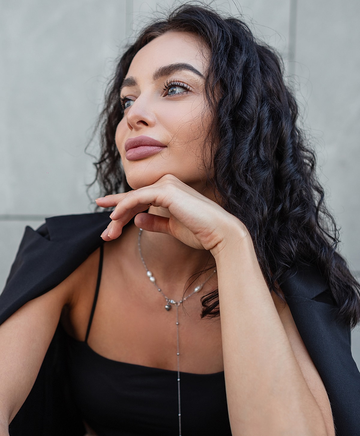 Woman posing thoughtfully in elegant black outfit.