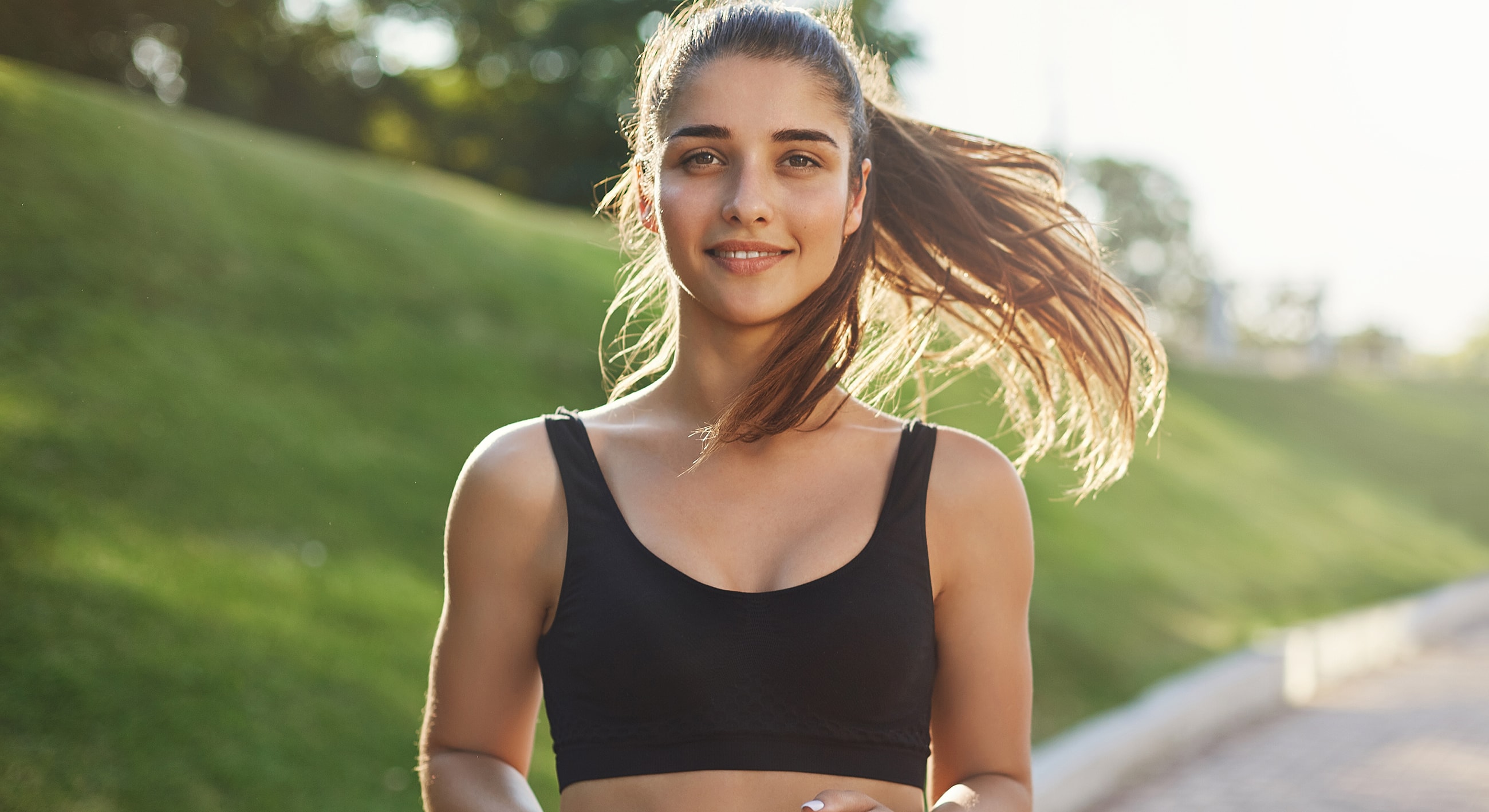 Smiling woman jogging outdoors in sunlight.