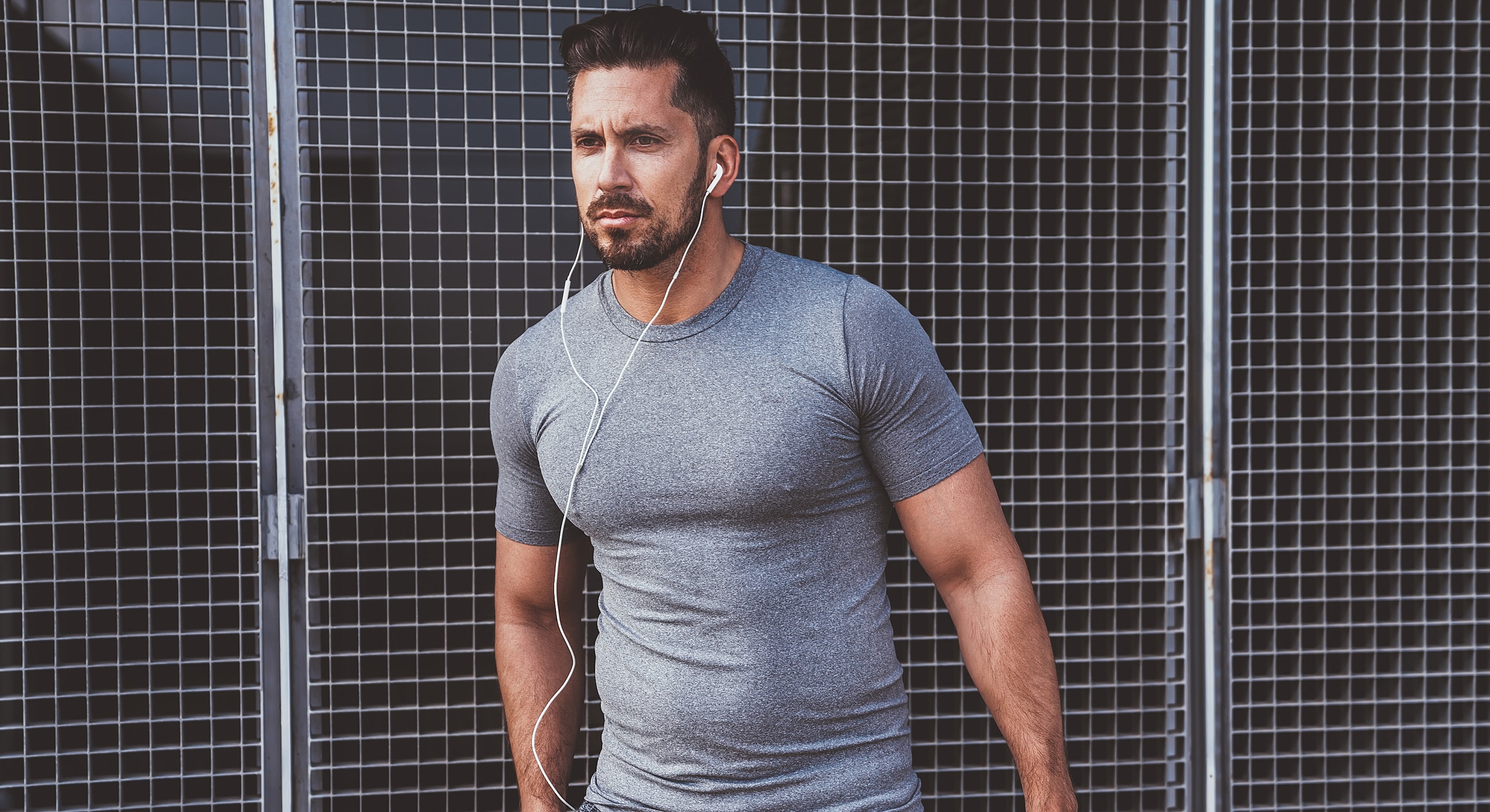 Man in gray shirt with headphones, standing outdoors.