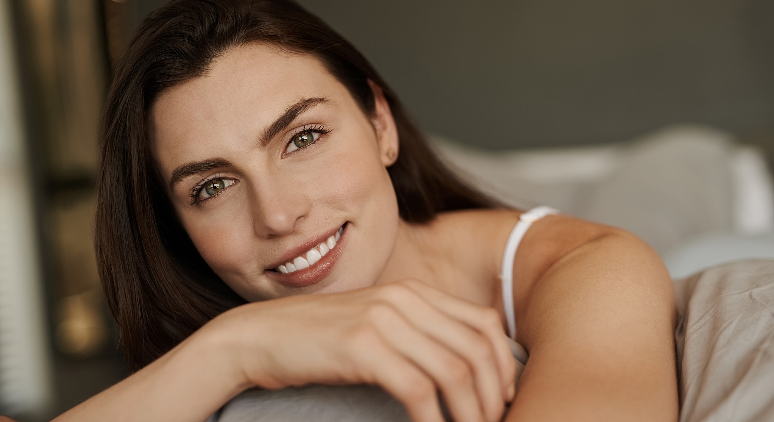 Smiling woman lying on bed, natural lighting.