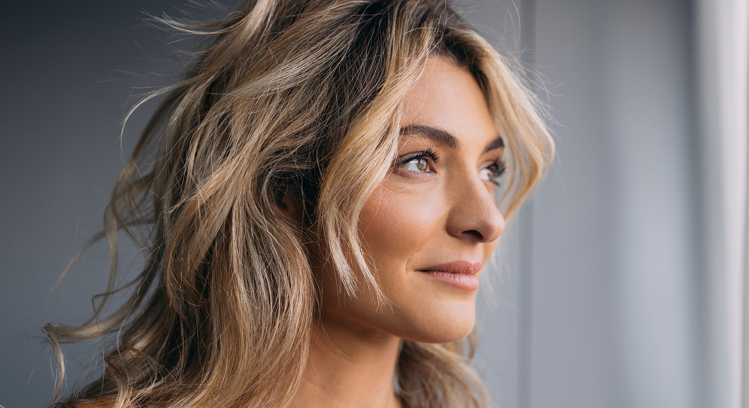 Woman with wavy hair looking thoughtfully outside.